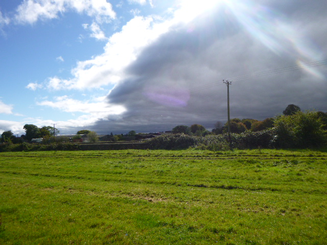 Green field under cloudy sky and sunbeam