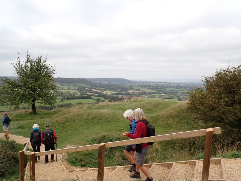 Hikers descending hill with scenic countryside view.