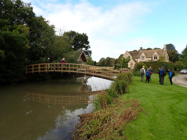 People walking by pond and bridge in countryside.