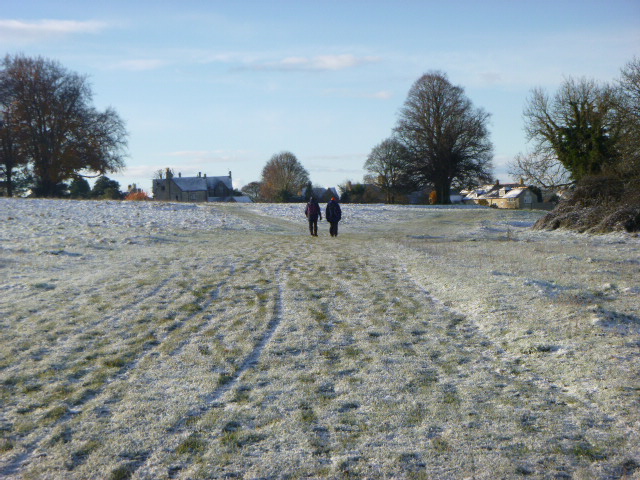 Two people walking on a frosty field path.