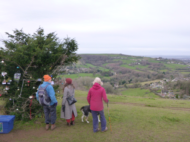 Three people and dog enjoy countryside view.