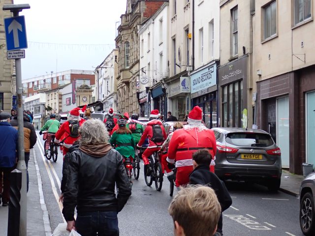 Cyclists in Santa outfits ride through city street.