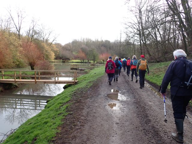 Group hiking along muddy trail beside river.